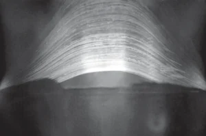 Fotografia em preto e branco de longa exposição, na qual centenas de finos arcos de luz claros atravessam o céu escuro em trajetórias paralelas e curvas, formando uma faixa densa acima de uma silhueta escura de construção na parte inferior da imagem